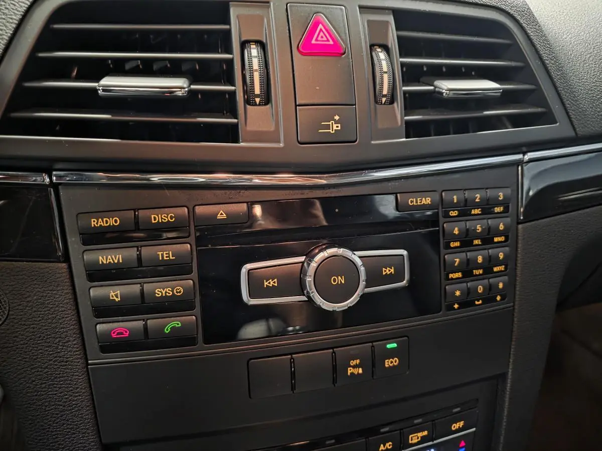 Console centrale noire de la Mercedes Classe E Coupé 2012 avec commandes radio, navigation et climatisation visibles en gros plan