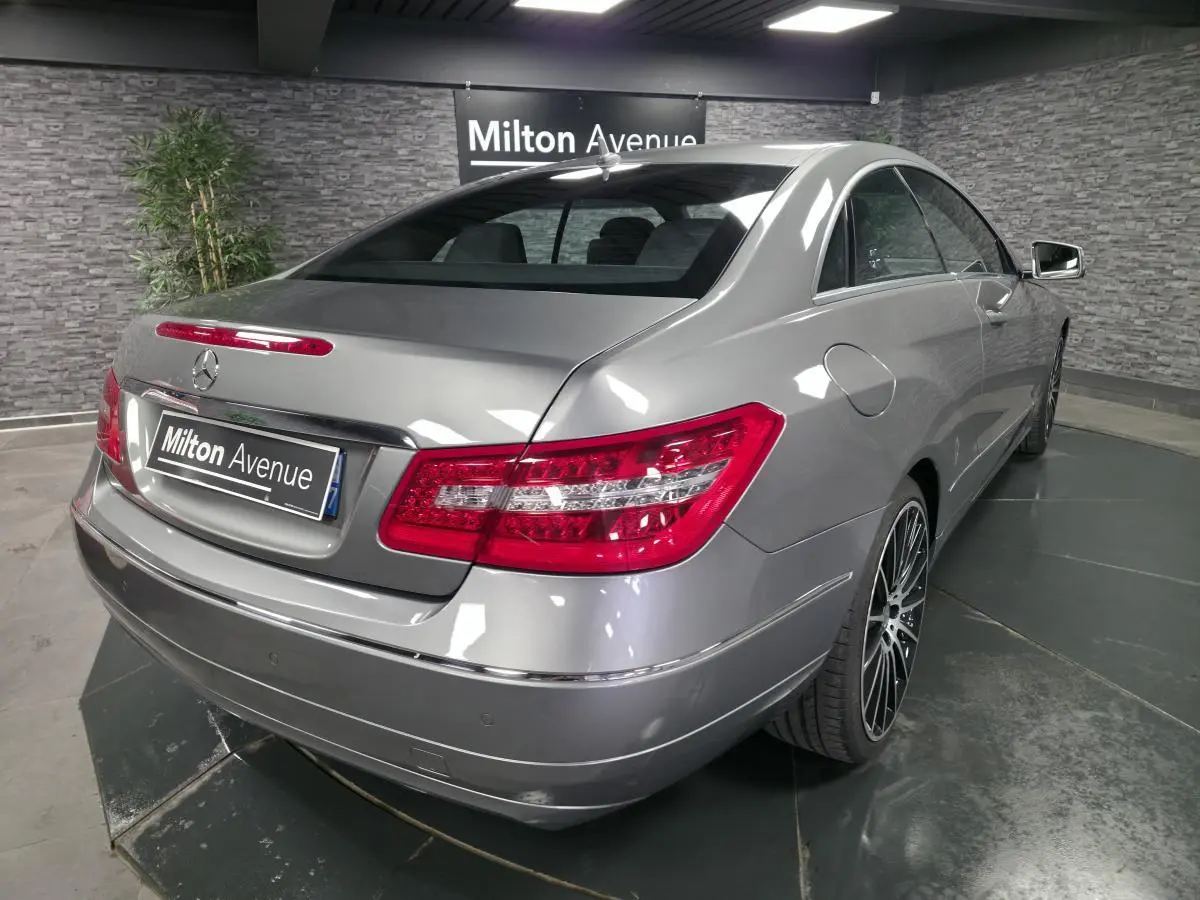 Vue 3/4 arrière droite d'une Mercedes Classe E Coupé gris métallisé avec jantes alliage 19 pouces dans un showroom.