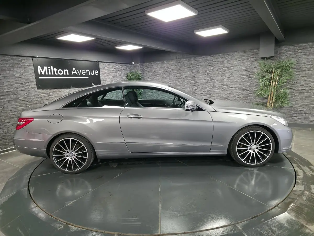 Profil côté gauche d'une Mercedes Classe E Coupé E 200 gris métallisé avec jantes alliage 19 pouces en intérieur showroom.