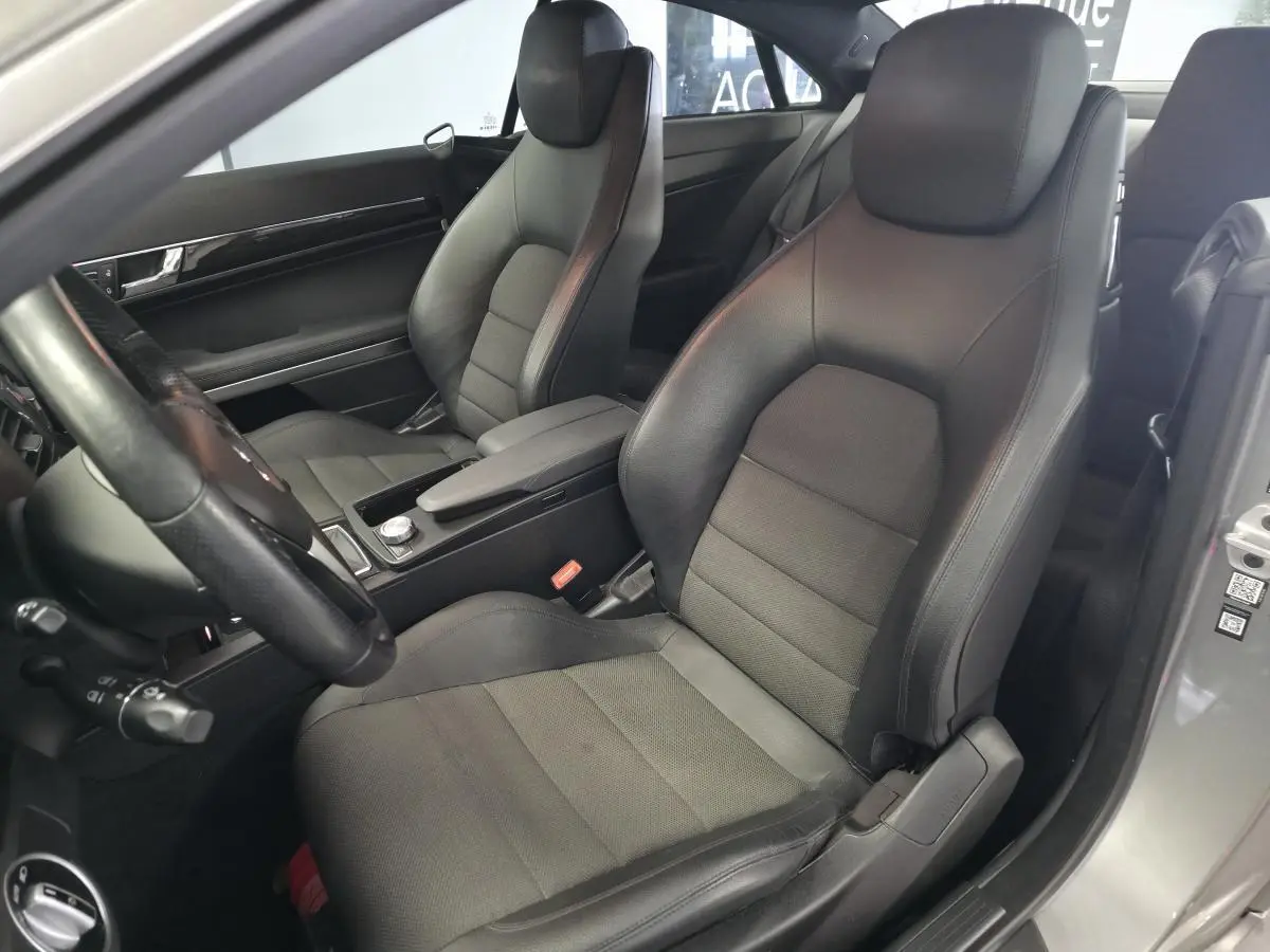 Vue intérieure côté conducteur du coupé Mercedes Classe E 200 gris, sièges en similicuir noir avec accoudoir central.