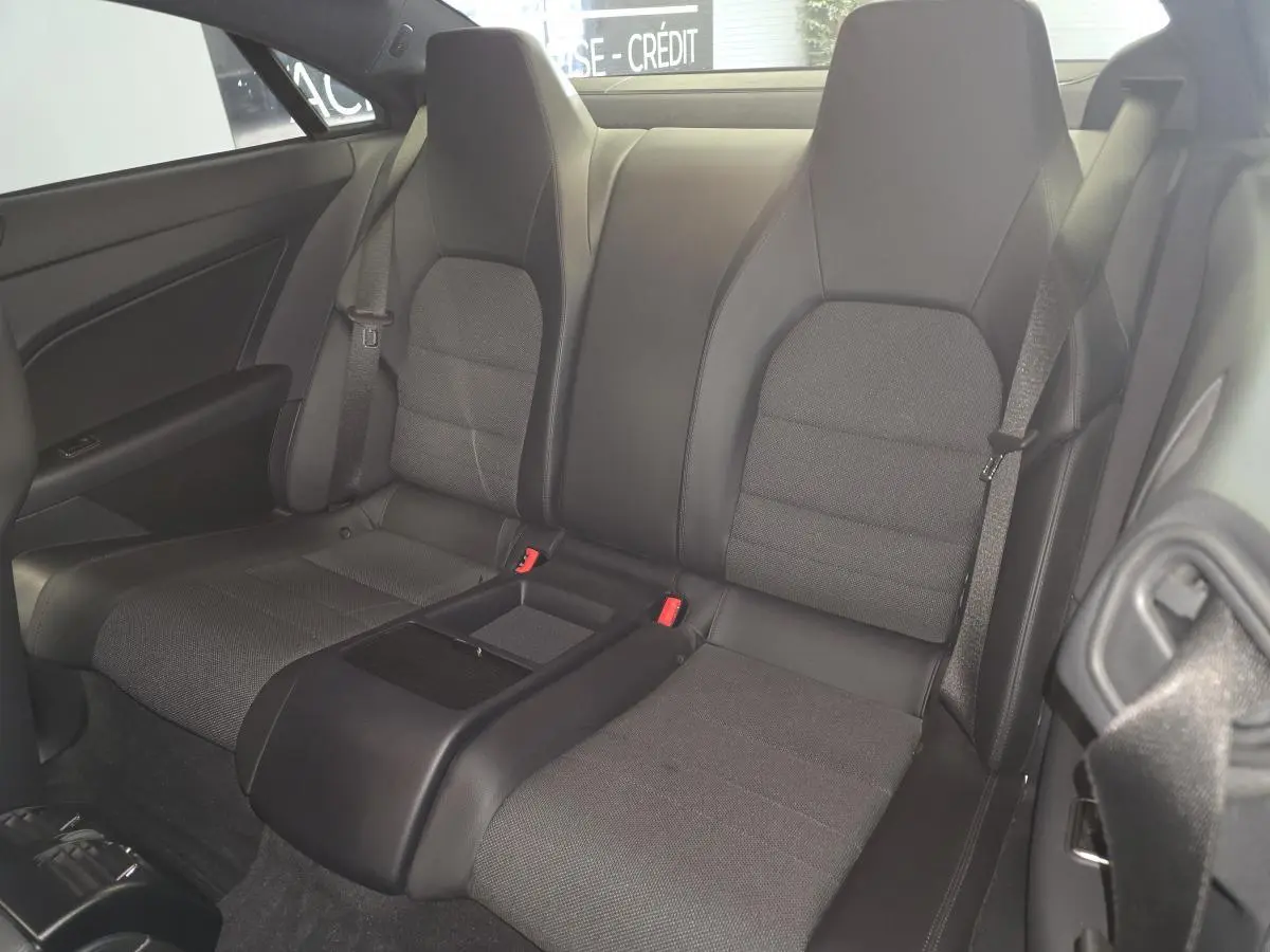 Vue arrière intérieure du coupé Mercedes Classe E 200 gris, montrant les sièges arrière en tissu et similicuir noir avec accoudoir central.