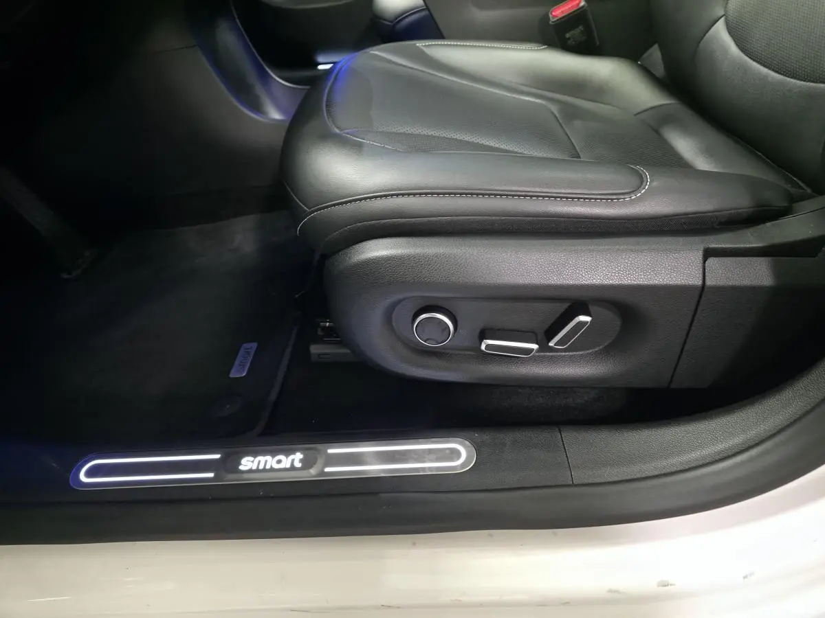 Gros plan sur le siège conducteur noir cuir et le seuil de porte blanc éclairé du logo Smart d'une Smart #1 électrique 2024.