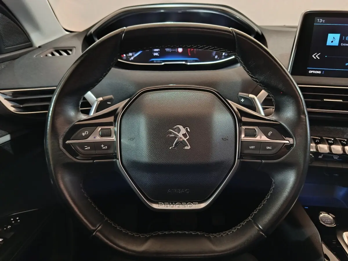 Vue rapprochée du volant cuir noir de la Peugeot 3008 avec commandes intégrées et tableau de bord numérique.
