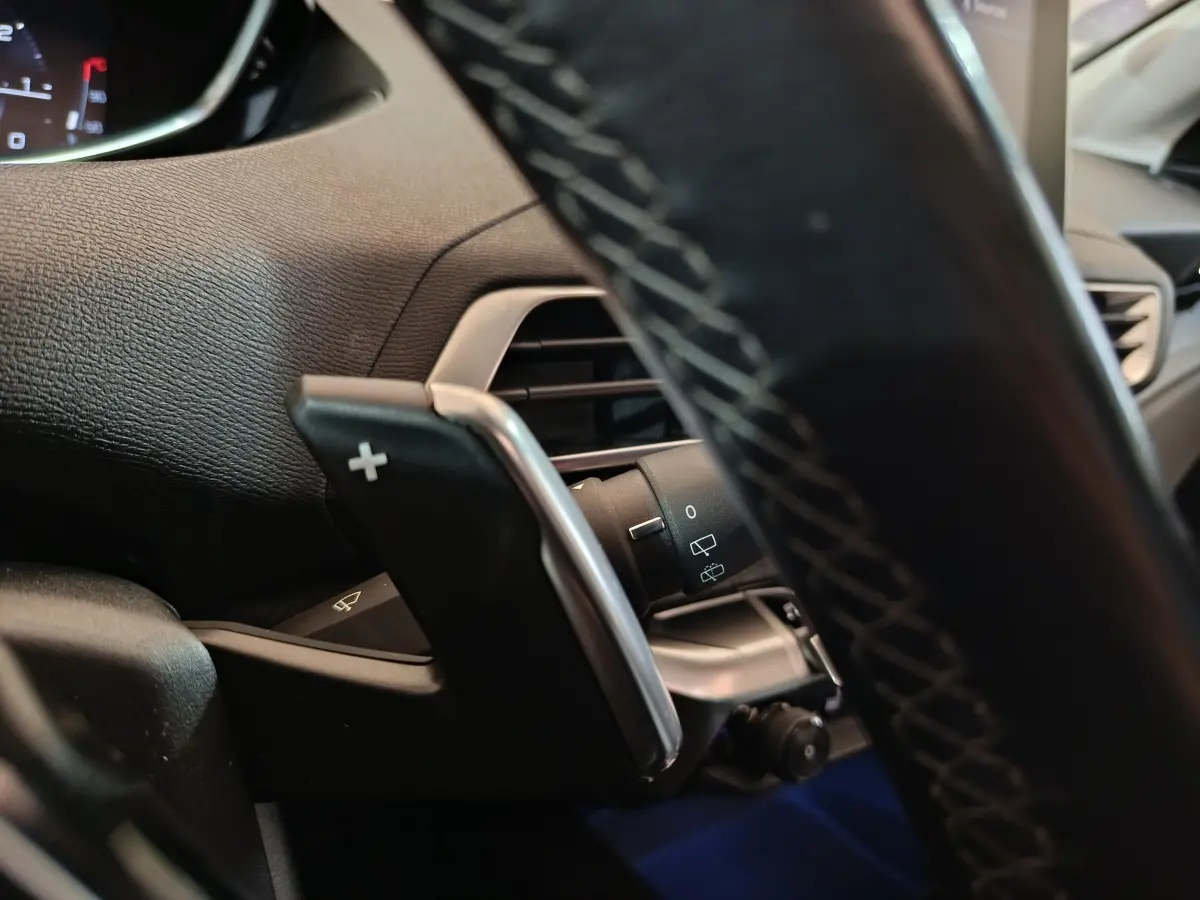 Gros plan sur la palette de changement de vitesse droite et partie du volant cuir noir du Peugeot 3008 blanc, intérieur avant.