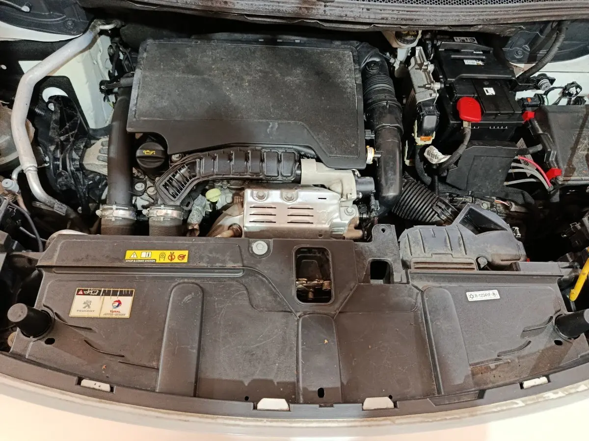Vue plongeante sur le moteur essence d’un Peugeot 3008 blanc, version Puretech 130 avec capot ouvert.