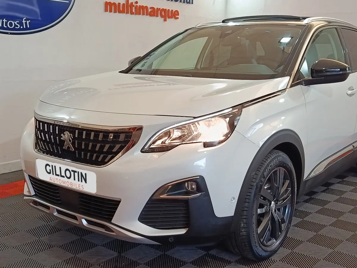Vue 3/4 avant droit d'un Peugeot 3008 blanc avec calandre noire et phares allumés en intérieur showroom.