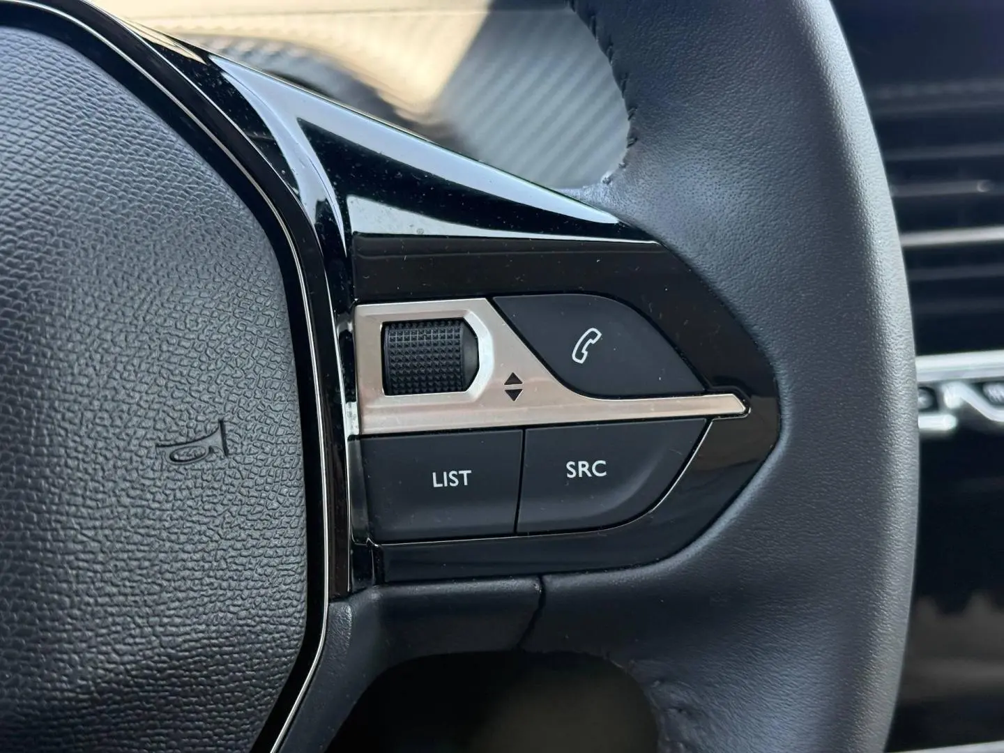 Gros plan sur les commandes audio au volant noir de la Peugeot 208 1.2 100ch Allure 2025.