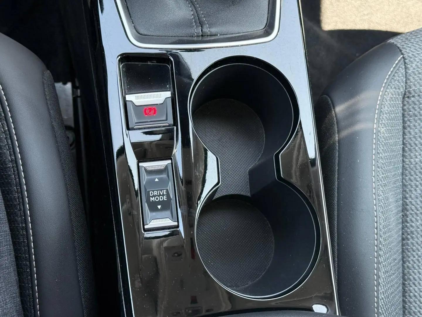 Vue plongeante sur la console centrale noire brillante de la Peugeot 208 gris Artense avec boutons frein à main et mode de conduite.