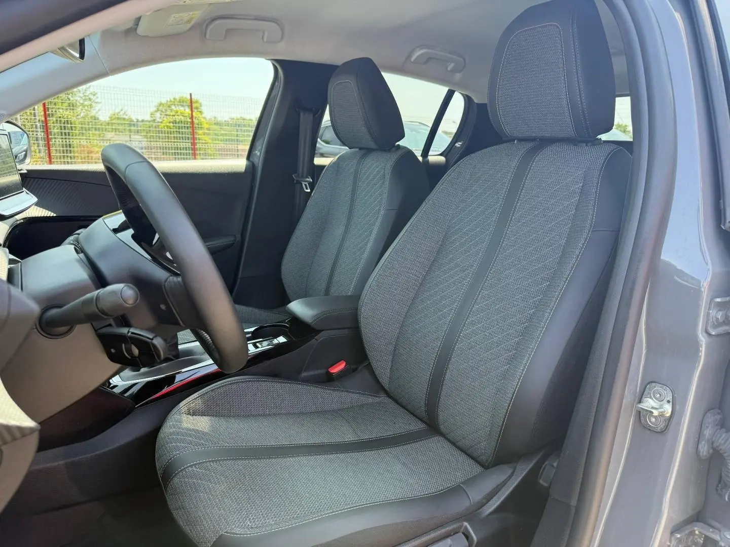 Vue intérieure côté conducteur de la Peugeot 208 1.2 100ch Allure gris Artense, sièges tissu gris avec accoudoir central.
