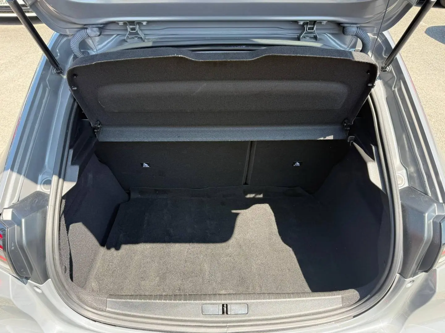 Coffre ouvert vu de dessus d'une Peugeot 208 gris Artense avec intérieur de coffre noir et banquette arrière rabattable.
