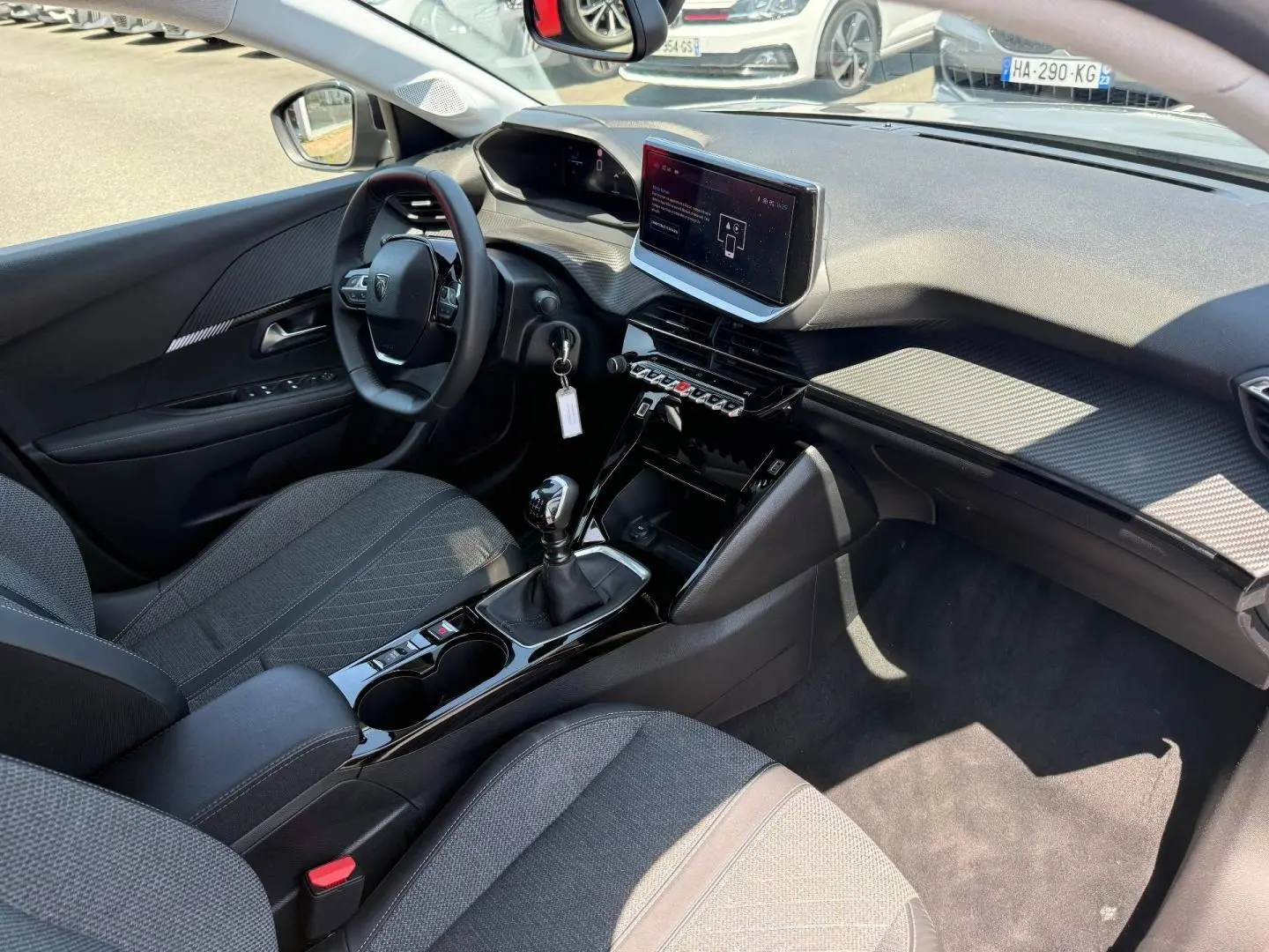 Vue intérieure côté conducteur de la Peugeot 208 1.2 100ch Allure avec tableau de bord moderne et sellerie tissu gris.