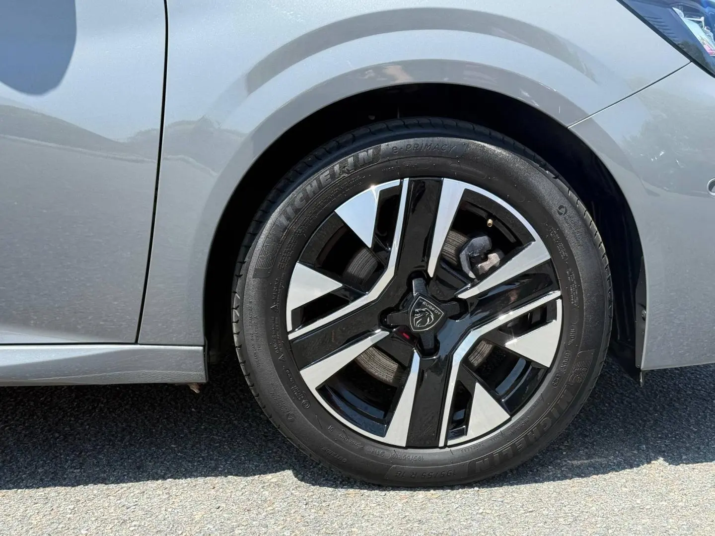 Gros plan sur la roue avant droite d'une Peugeot 208 gris Artense avec jante alu bicolore noire et argent.
