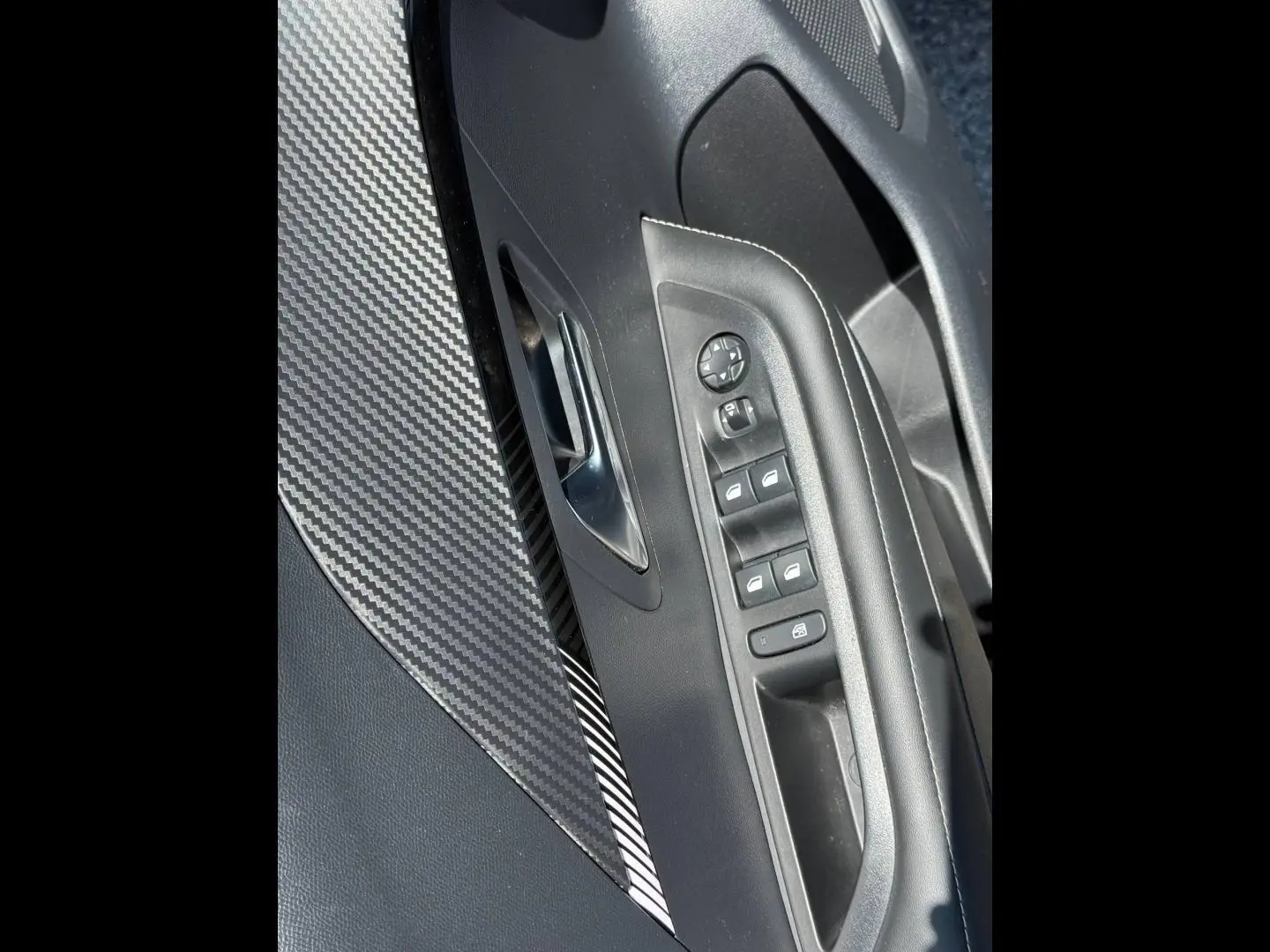 Gros plan sur la porte avant gauche de la Peugeot 208 gris Artense, avec commandes électriques et insert effet carbone.