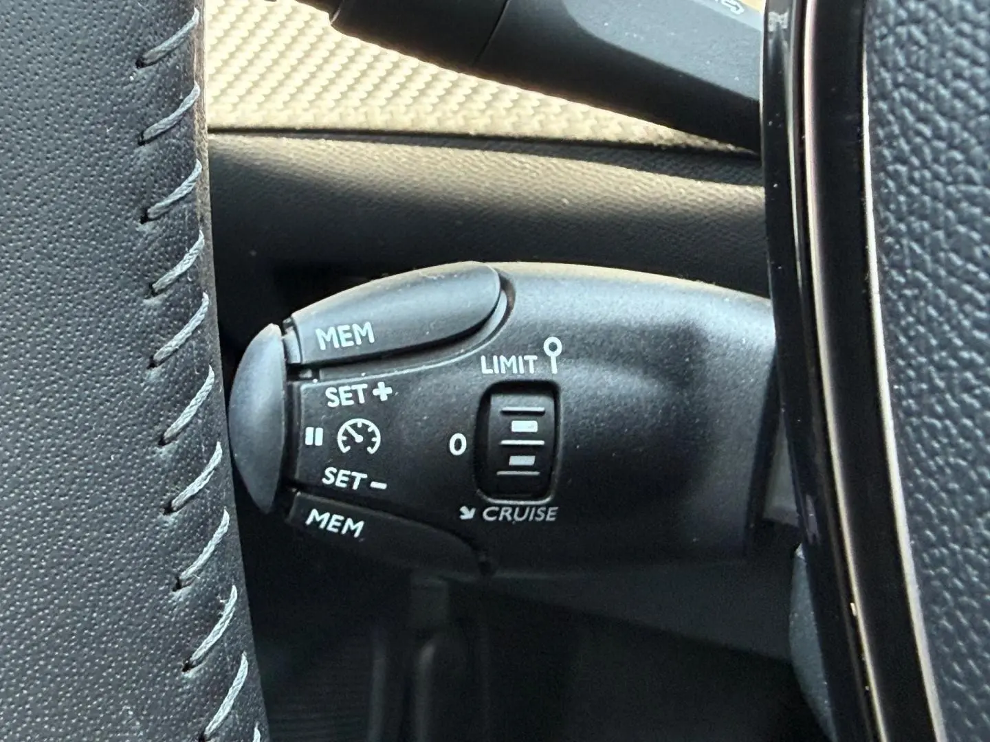 Gros plan sur la commande du régulateur de vitesse au volant d’une Peugeot 208 gris Artense, intérieur noir.