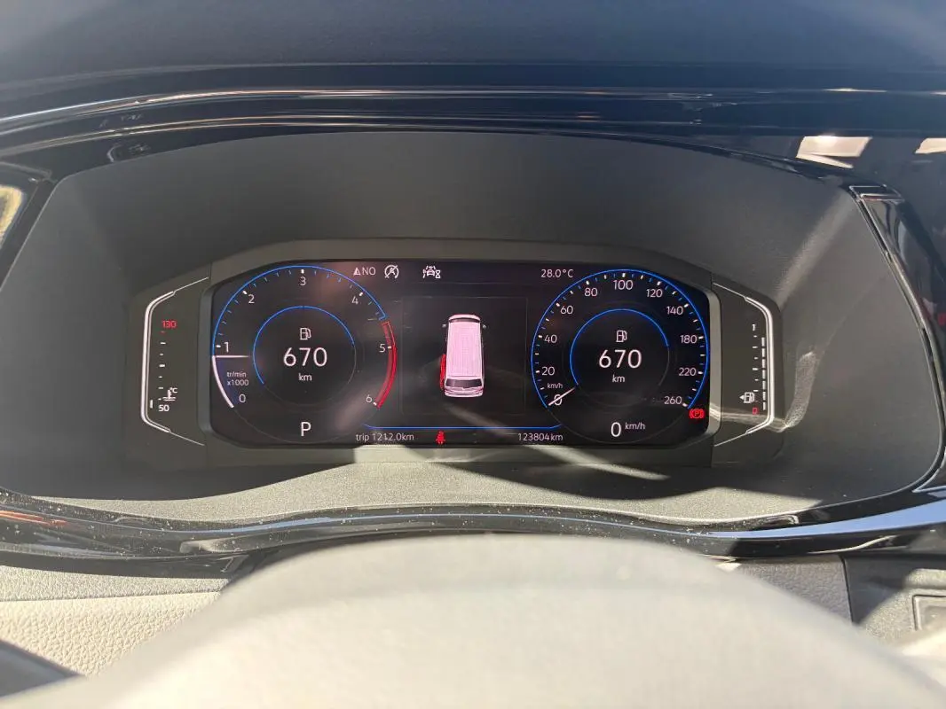 Vue rapprochée du tableau de bord numérique du Volkswagen Transporter blanc, affichant 670 km d'autonomie et 28°C.