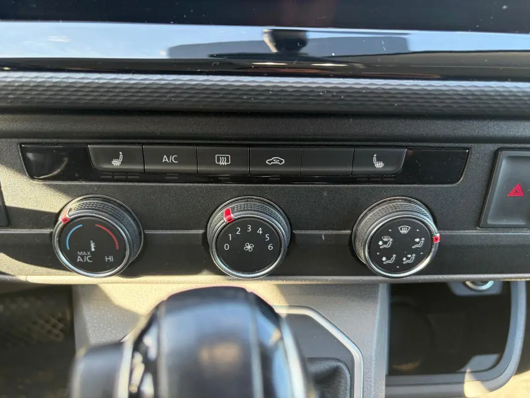 Gros plan sur les commandes de climatisation et ventilation du Volkswagen Transporter blanc, avec boutons rotatifs et indicateurs rouges.