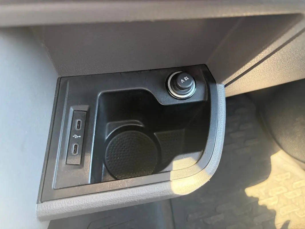 Gros plan sur la prise 12V et les deux ports USB-C dans le rangement central du Volkswagen Transporter blanc.