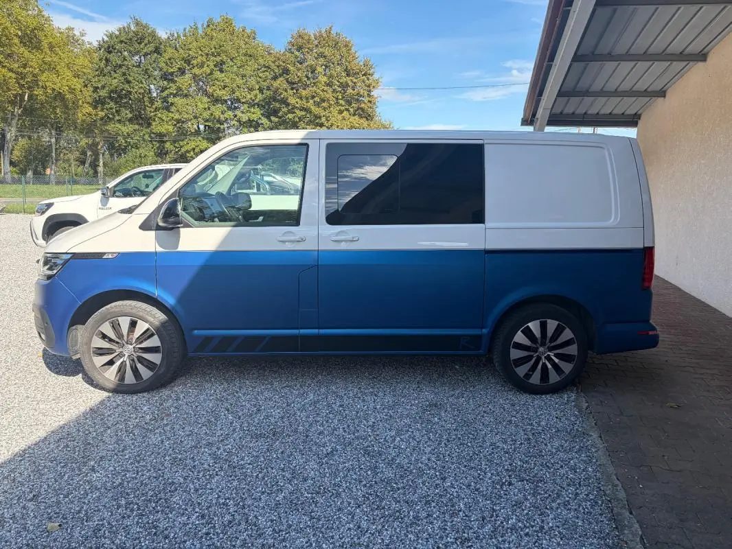 Vue de profil côté gauche d’un Volkswagen Transporter 2.0 TDI blanc et bleu, avec jantes aluminium et vitres teintées.