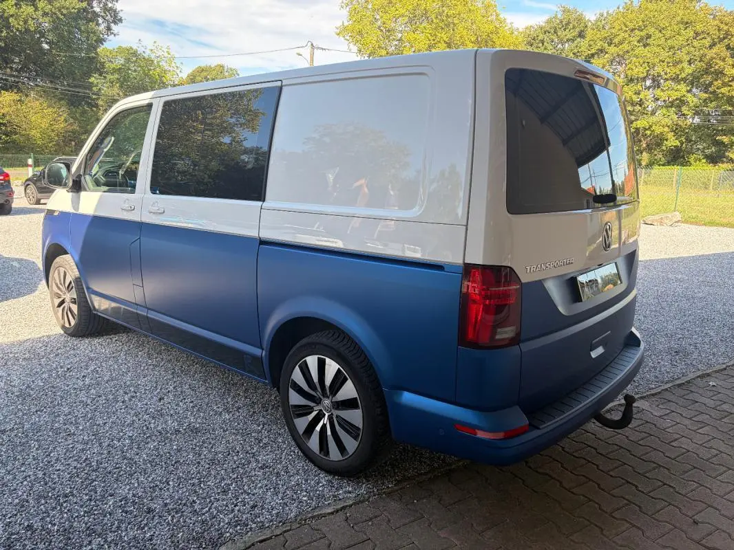 Vue 3/4 arrière droit d'un Volkswagen Transporter 2 tons blanc et bleu avec jantes aluminium et vitres teintées.