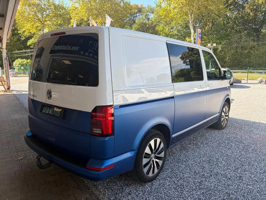 Vue 3/4 arrière droite d’un Volkswagen Transporter 2.0 TDI blanc et bleu avec jantes aluminium et vitres teintées.