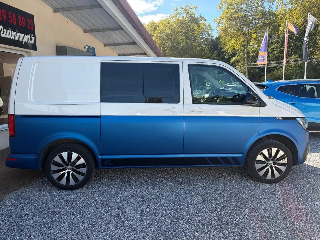 Vue de profil droit d’un Volkswagen Transporter bicolore blanc et bleu, avec jantes aluminium et vitres teintées.