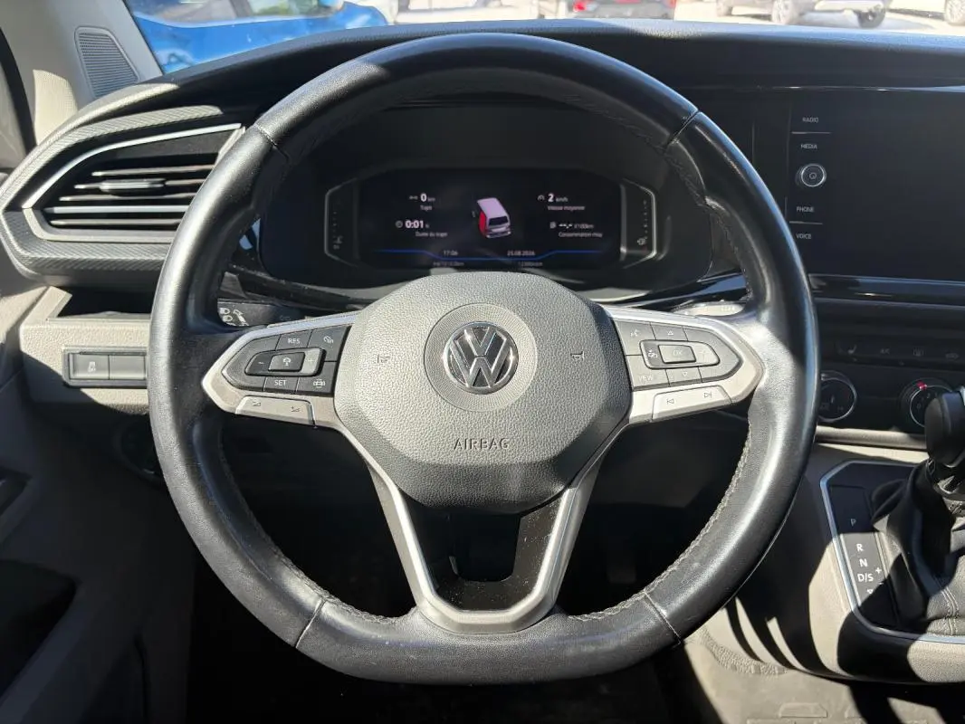Vue rapprochée du volant cuir noir de Volkswagen Transporter 2020 avec commandes multifonctions et tableau de bord digital.