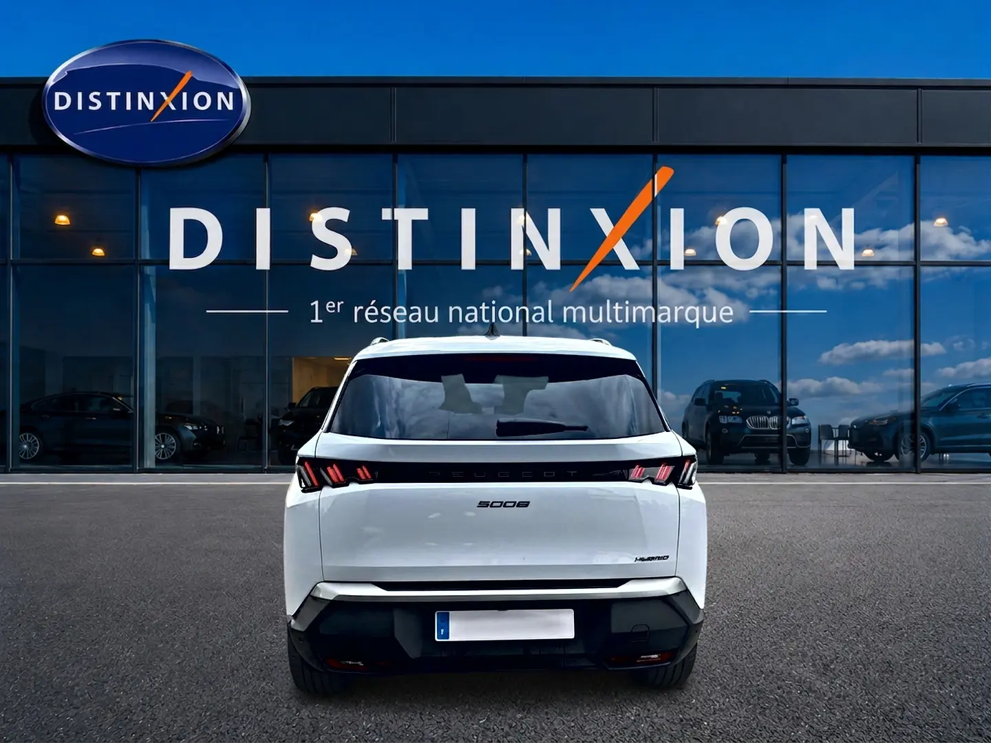 Vue arrière d’un Peugeot 5008 Hybrid blanc garé devant une vitrine avec logo Distinxion.