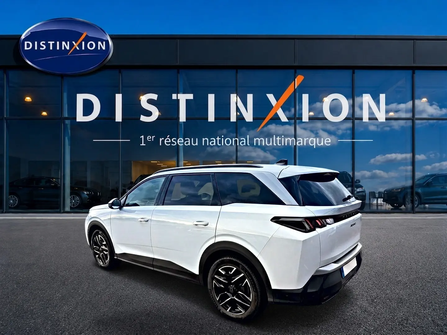 Peugeot 5008 blanc en 3/4 arrière droit, avec jantes alu noires et vitres arrière surteintées devant showroom Distinxion.