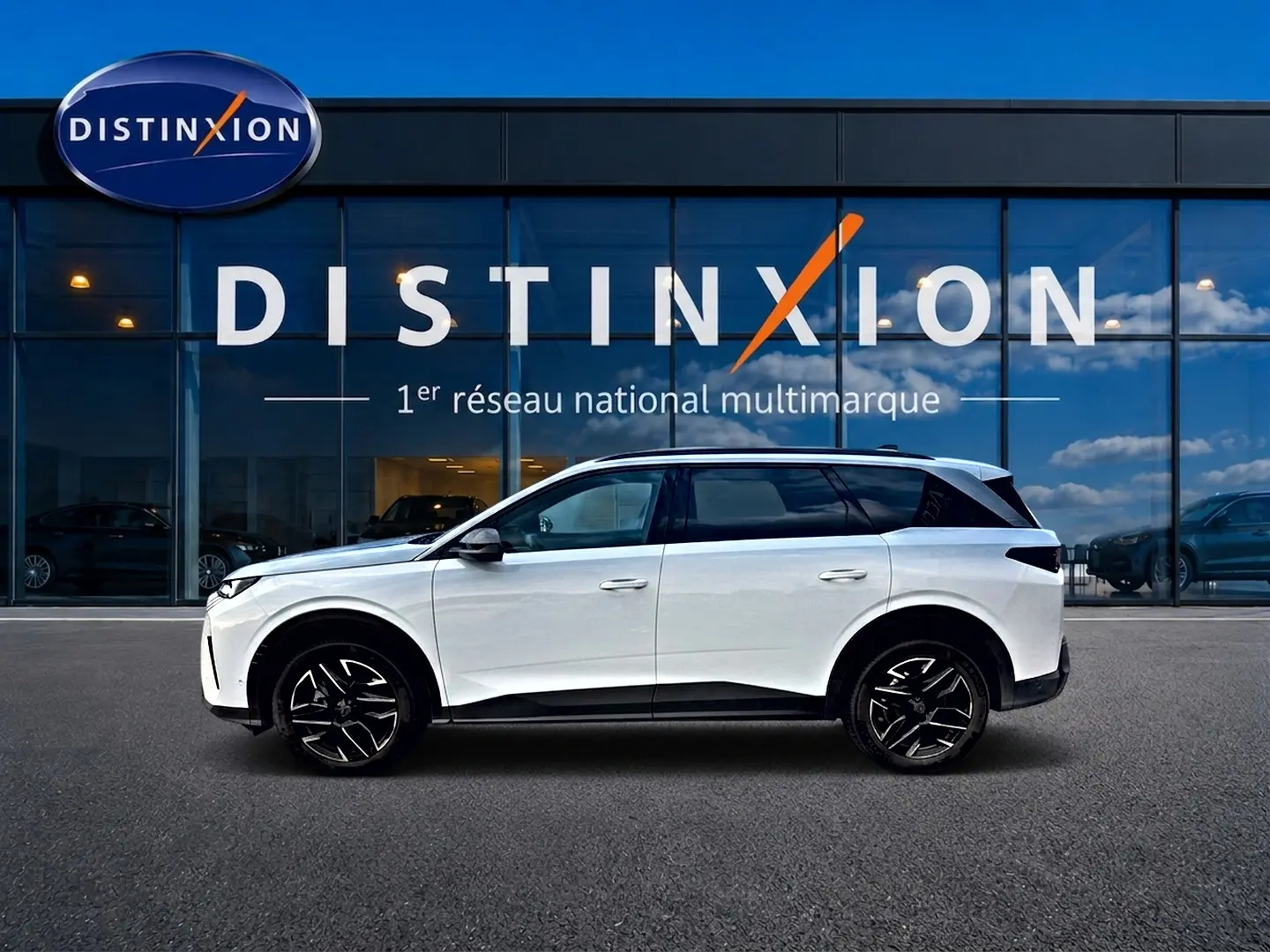 Vue de profil côté gauche d'un Peugeot 5008 blanc garé devant une vitrine avec logo Distinxion.