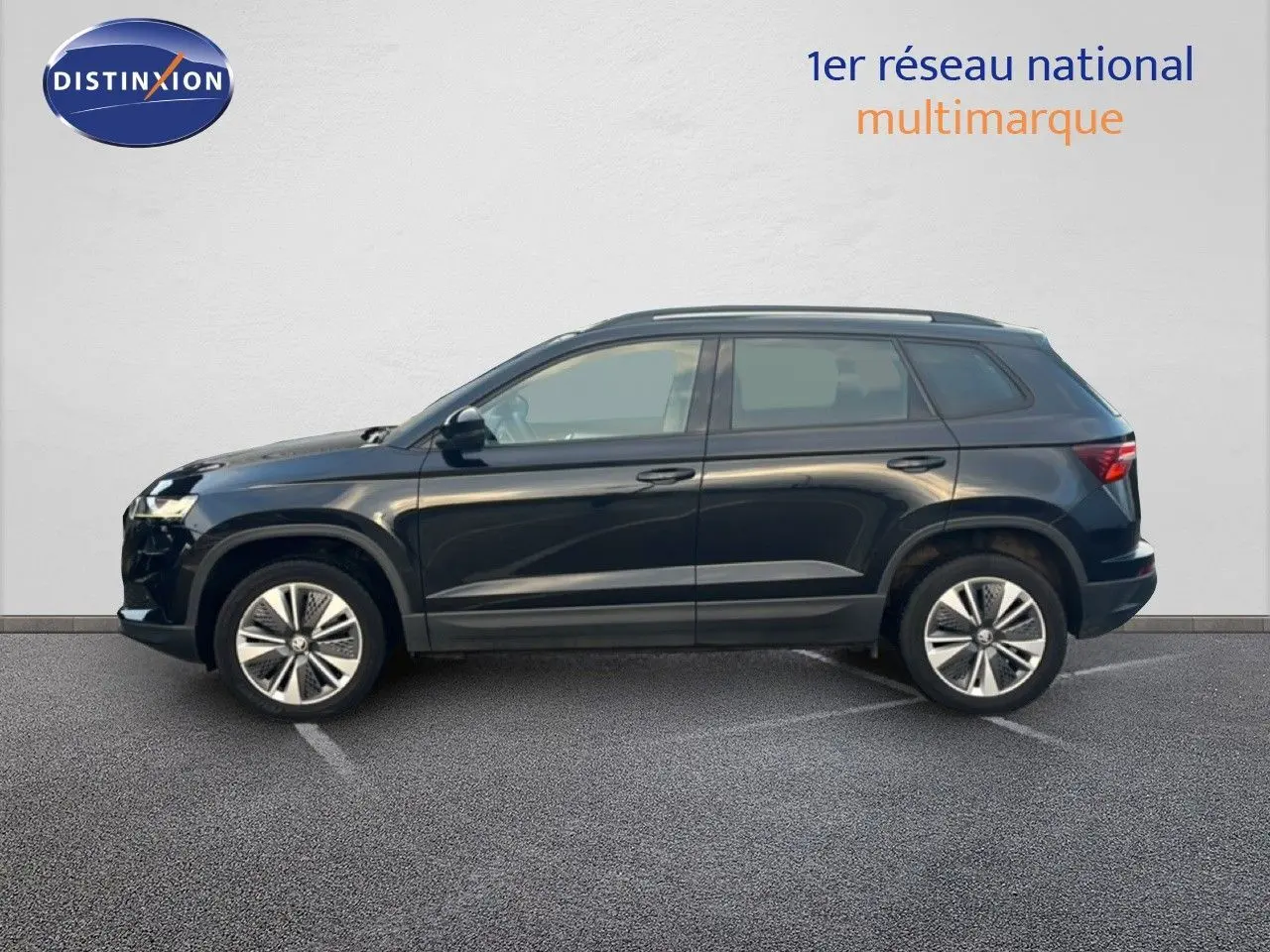 Profil côté gauche d'un Škoda Karoq noir Magic Metal 2023 garé devant un mur blanc, roues alliage bicolore visibles.