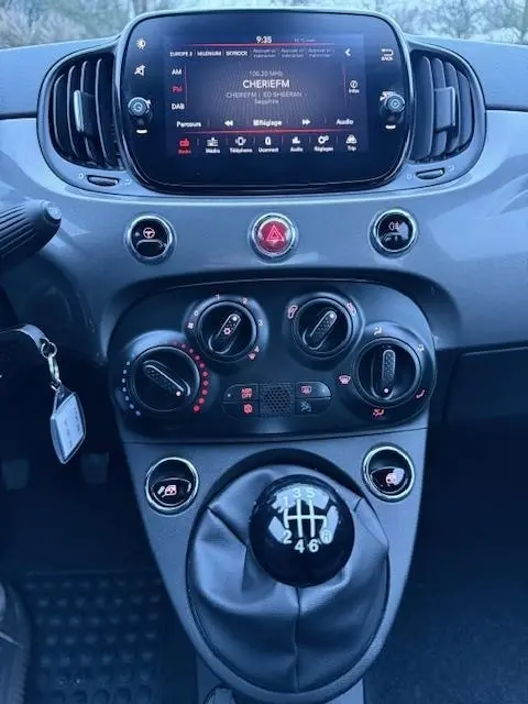 Vue rapprochée du tableau de bord et levier de vitesse manuel de la FIAT 500 Hybrid gris foncé avec écran tactile central allumé.