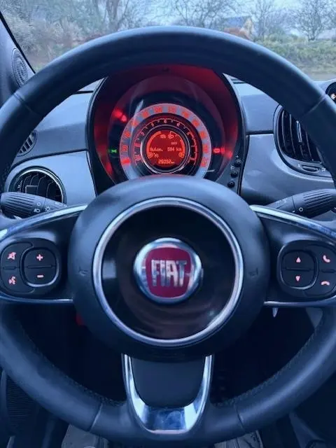 Vue rapprochée du volant noir FIAT avec tableau de bord central éclairé en rouge dans une FIAT 500 Hybrid 2022.