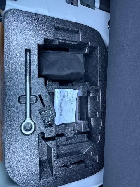Gros plan sur le rangement en mousse noir dans le coffre d'une FIAT 500 gris foncé, avec outils et notice visibles.