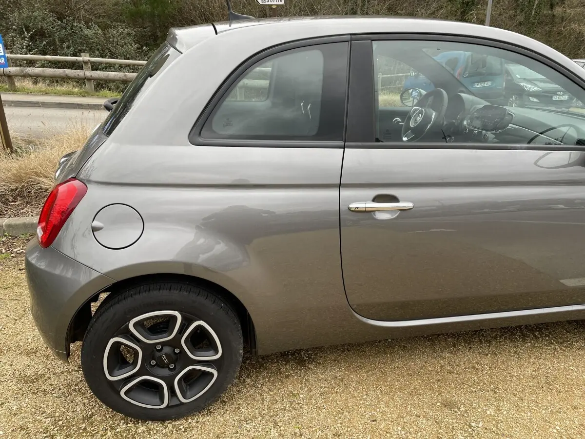 Vue latérale gauche d'une FIAT 500 Hybrid gris foncé, mettant en valeur la roue avant et la poignée de porte chromée.