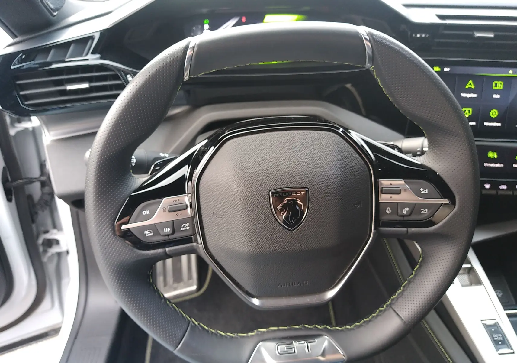 Vue rapprochée du volant cuir perforé avec surpiqûres vertes et logo GT du Peugeot 408 Hybrid 2024 blanc Okenite.
