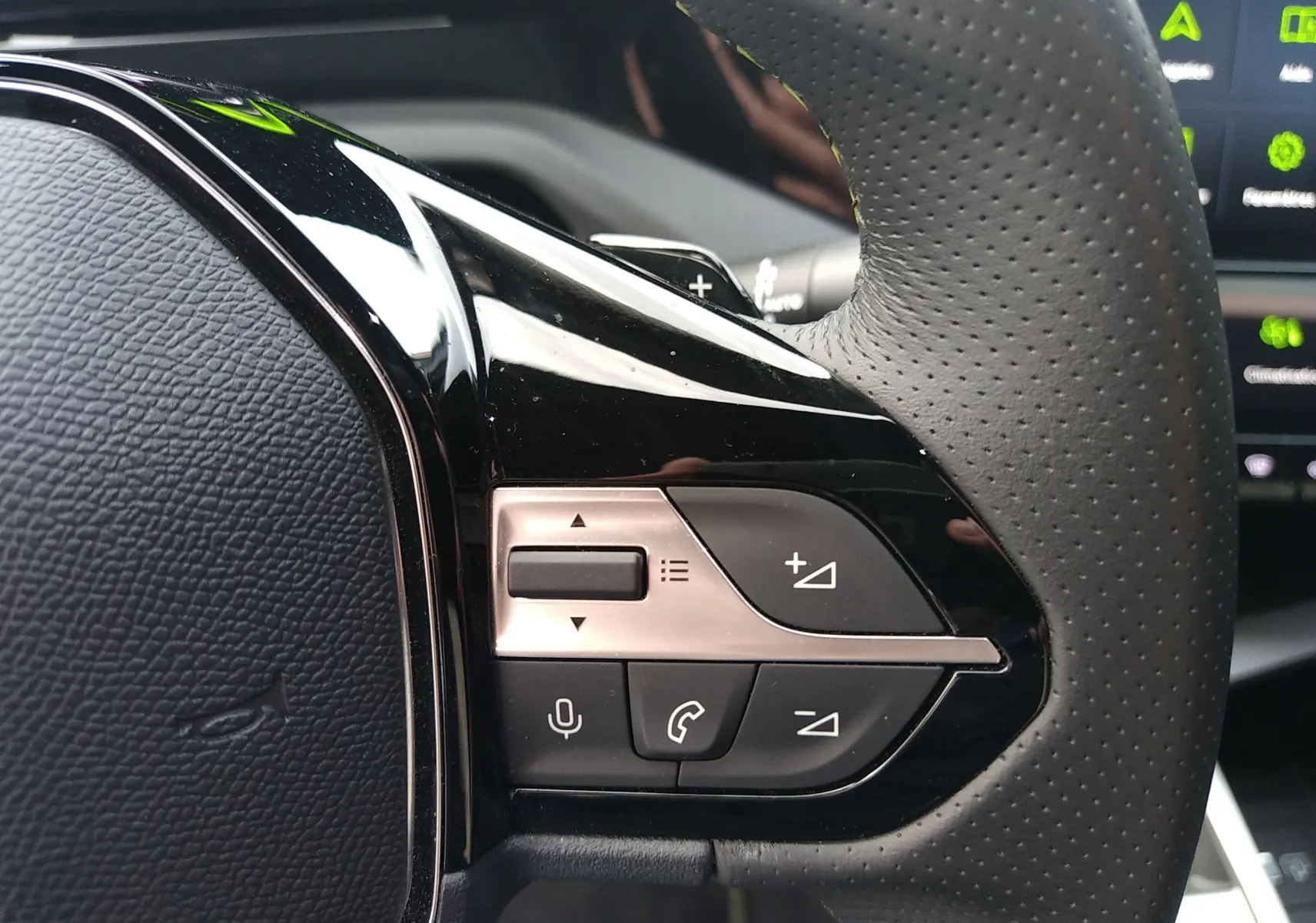 Gros plan sur les commandes multifonctions en plastique noir et argent du volant perforé d’un Peugeot 408 Hybrid 2024.