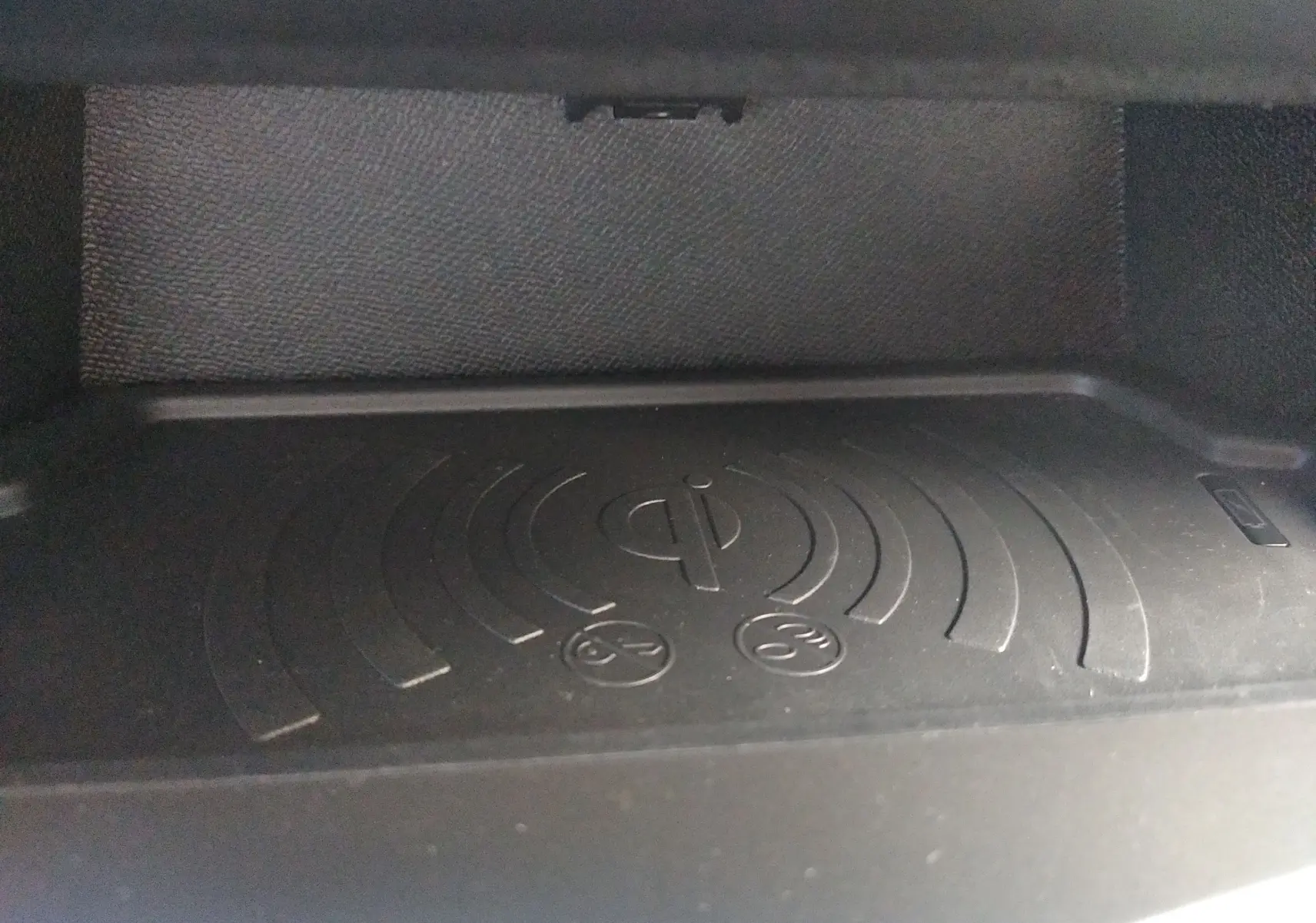 Gros plan sur le chargeur sans fil intégré dans la console centrale de la Peugeot 408 Hybrid blanche.