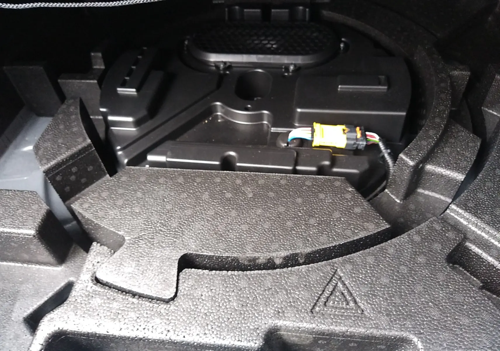 Détail du rangement sous le coffre de la Peugeot 408 Hybrid blanc Okenite, montrant le compartiment technique et câblage.