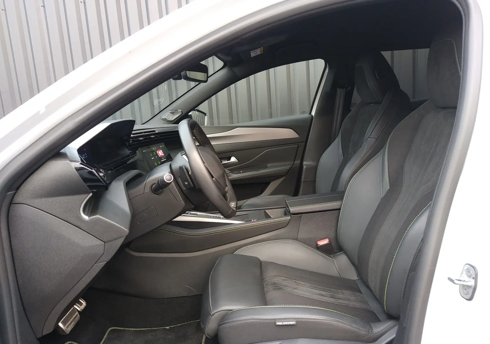 Vue intérieure côté conducteur de la Peugeot 408 Hybrid 136ch GT blanche, avec sièges sport en cuir et alcantara noirs.