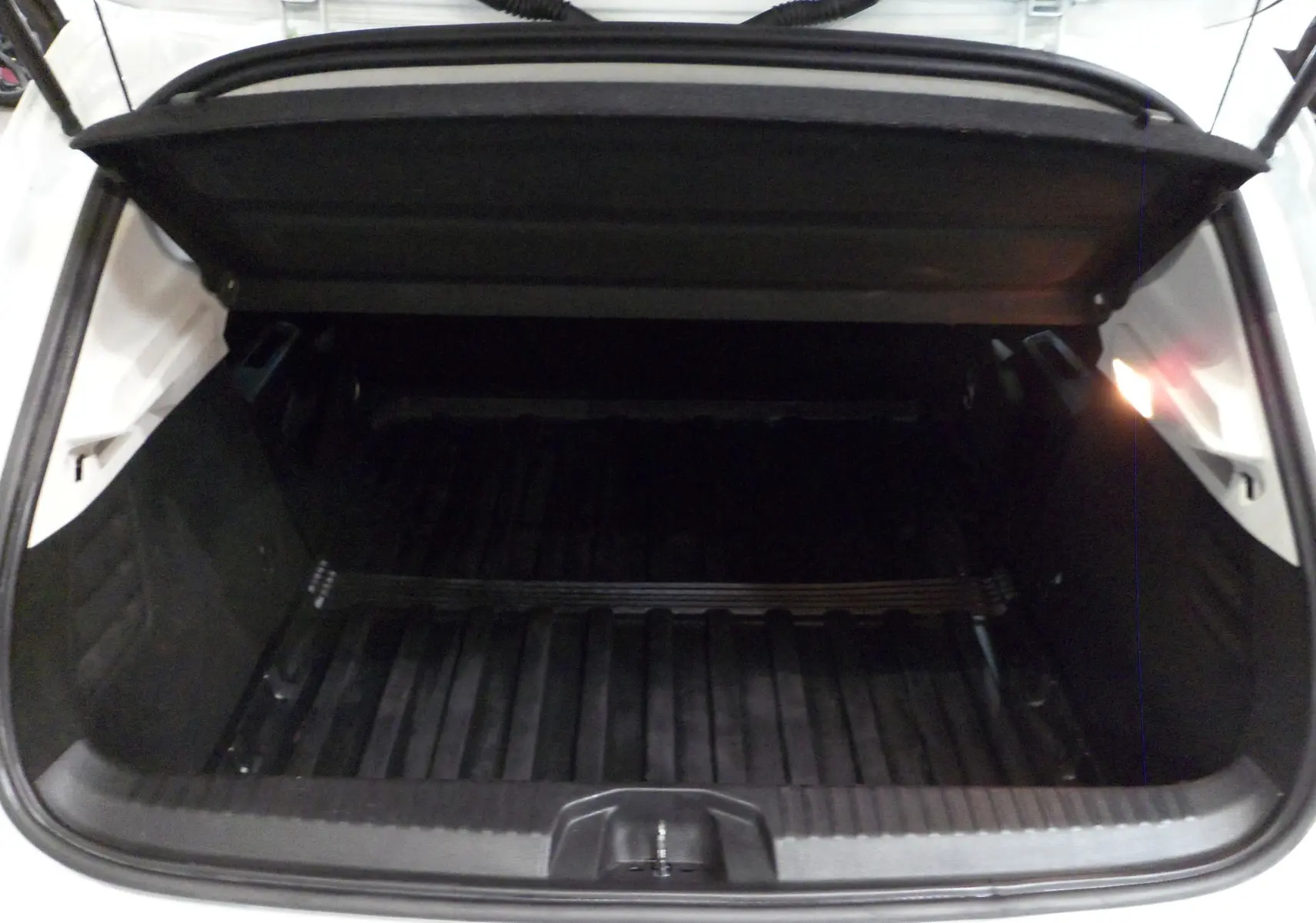 Coffre ouvert de la Renault Clio V Société blanc glacier, montrant un espace de chargement vide et protégé.