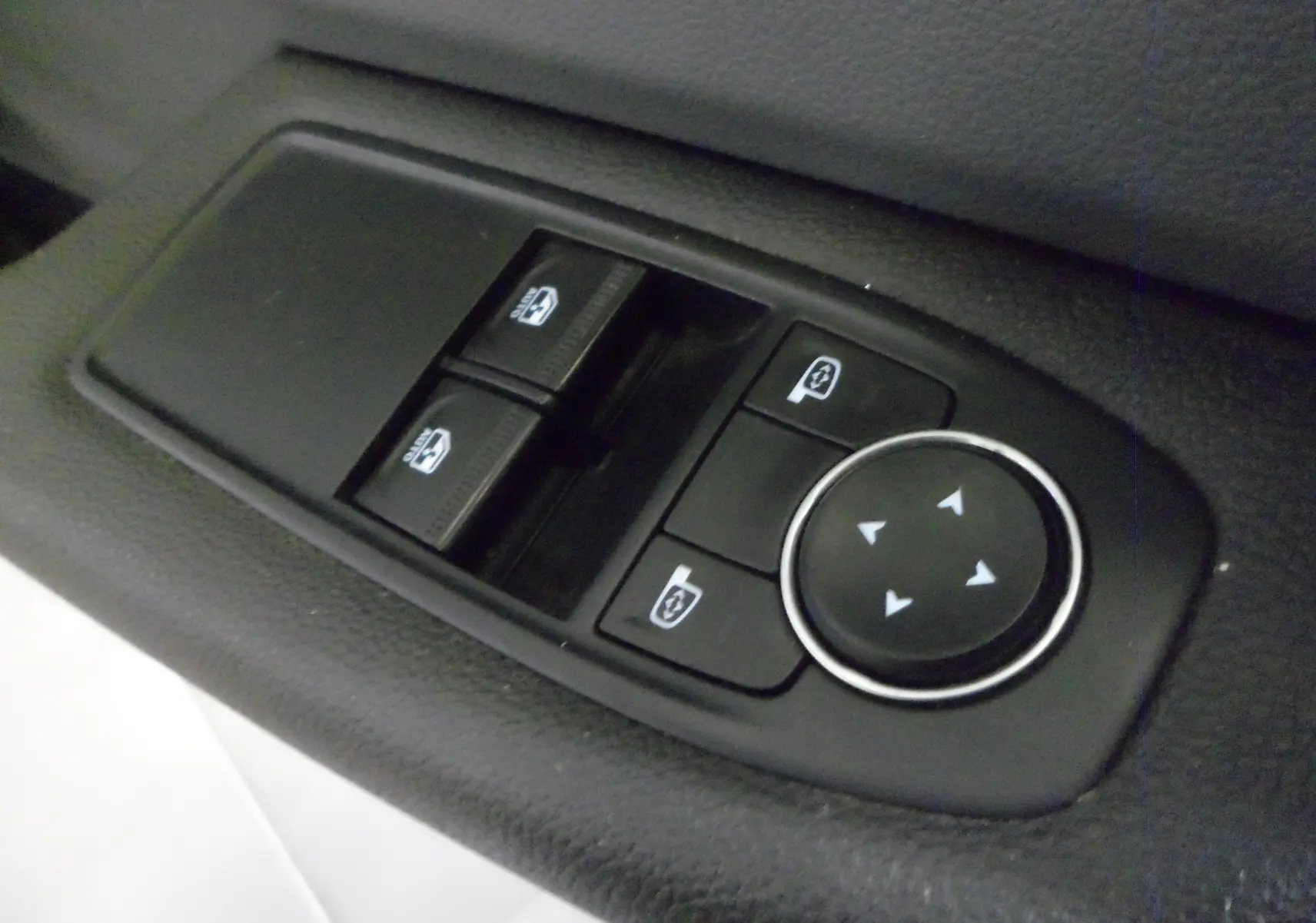 Gros plan sur les commandes électriques des vitres et des rétroviseurs côté conducteur d'une Renault Clio V blanche.