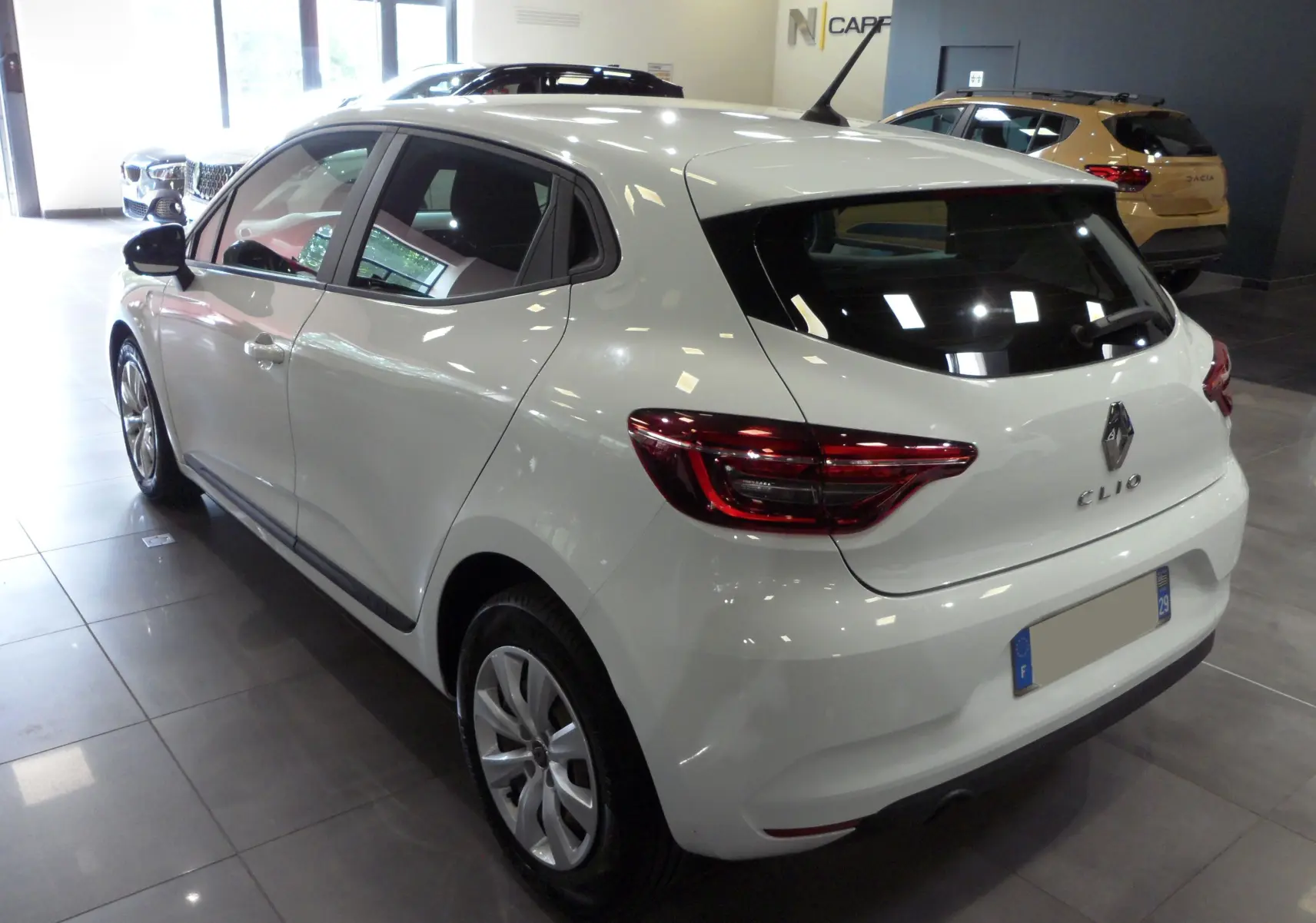Renault Clio V blanc glacier vue 3/4 arrière droit en intérieur, avec feux arrière LED et jantes alliage.