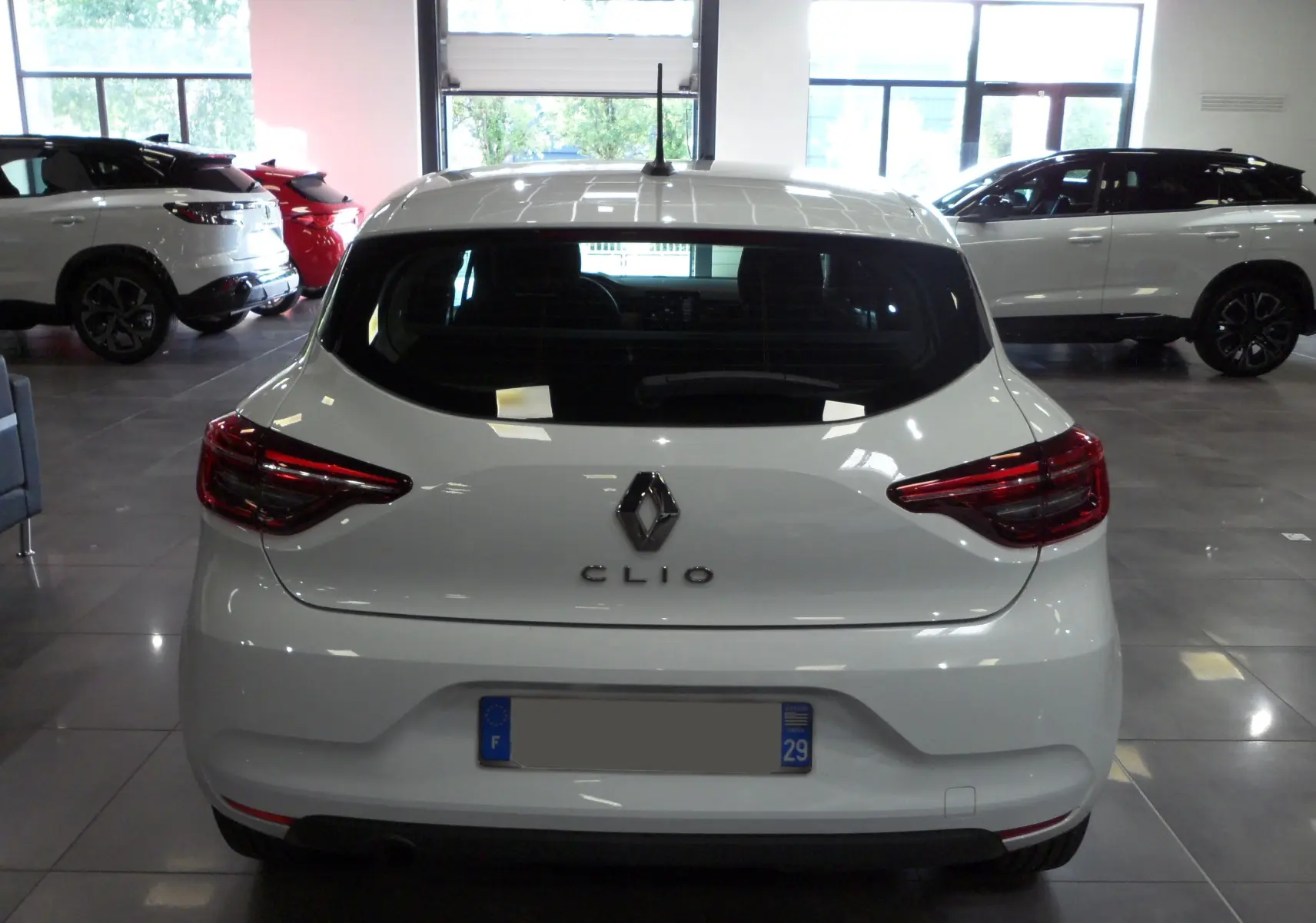 Vue arrière d'une Renault Clio V blanche Glacier en showroom, mettant en valeur ses feux arrière et son logo distinctif.