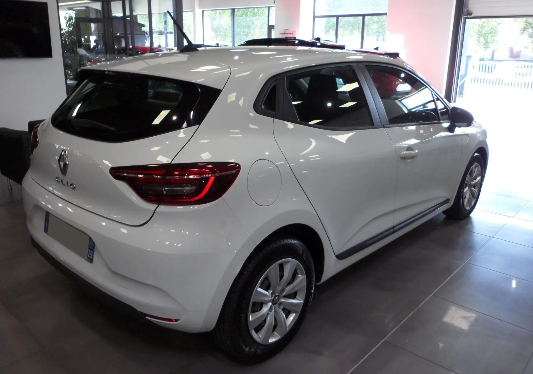 Renault Clio V blanche vue en 3/4 arrière droit dans un showroom, avec feux arrière LED et jantes alliage.