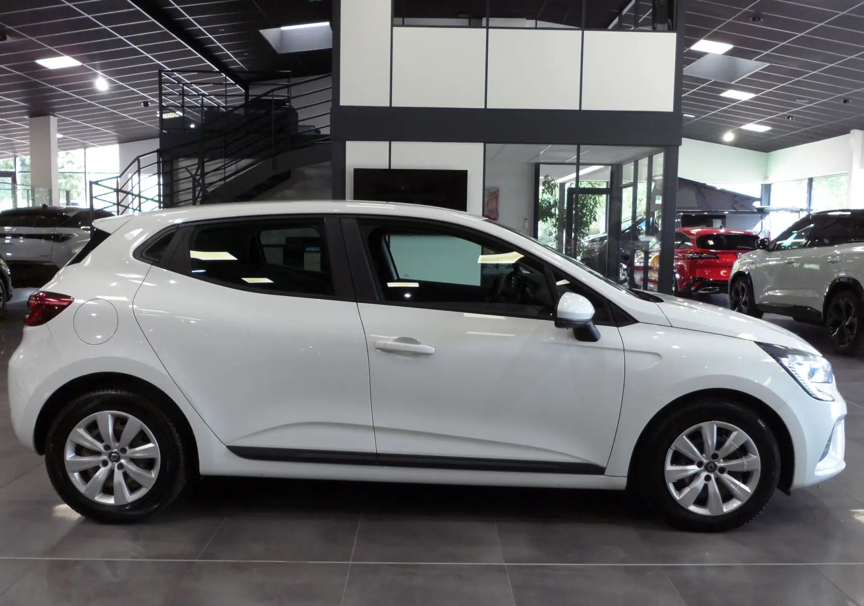 Profil côté gauche d'une Renault Clio V blanche Glacier en version Société, visible en intérieur showroom moderne.