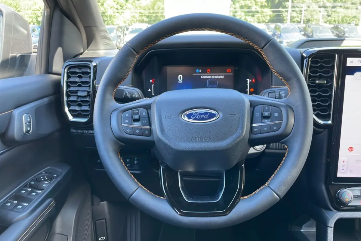 Vue intérieure centrée sur le volant noir à surpiqûres marron du Ford Ranger 2025 gris carbone avec tableau de bord numérique.