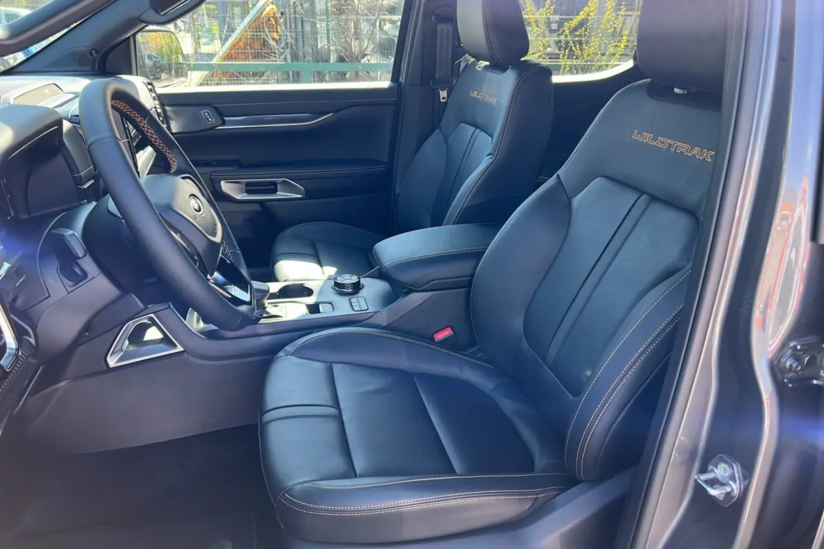 Intérieur du Ford Ranger 2025 gris carbone, vue côté conducteur, sièges cuir noirs avec surpiqûres orange Wildtrak.