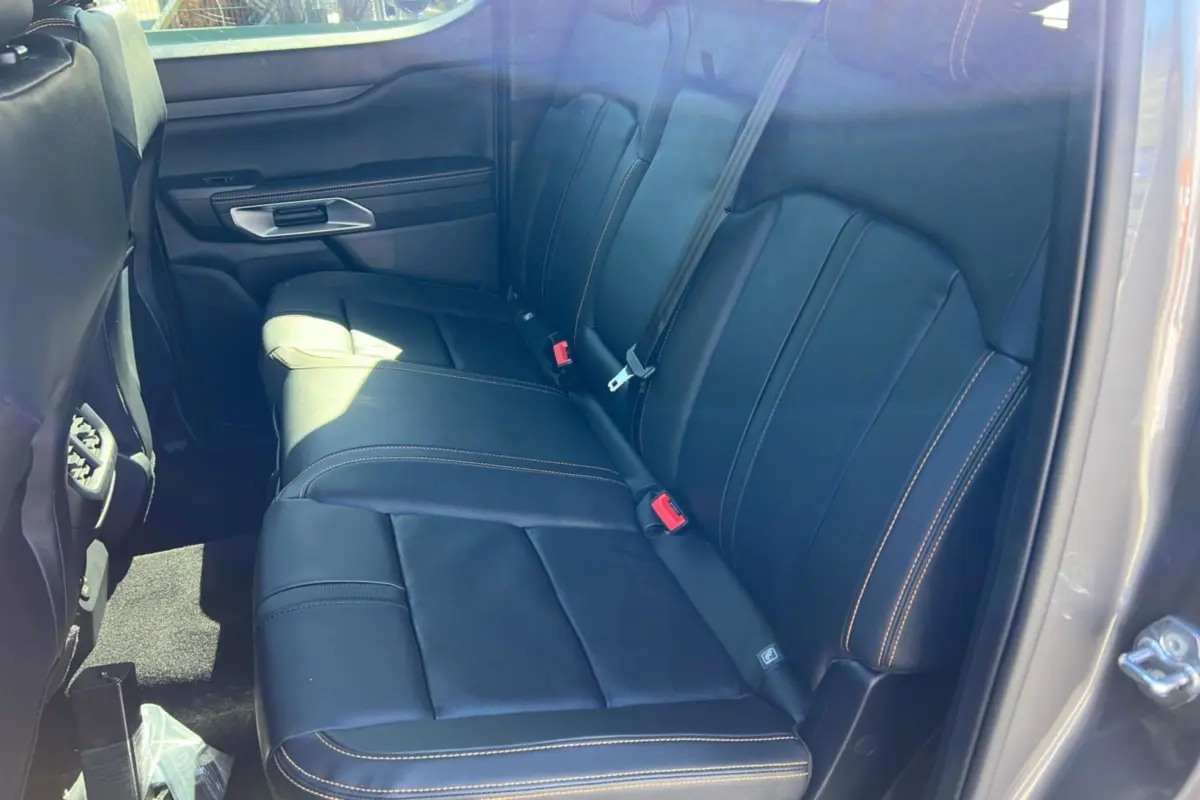Vue intérieure côté arrière droit du Ford Ranger 2025 gris carbone, sièges en cuir noir avec surpiqûres orange visibles.