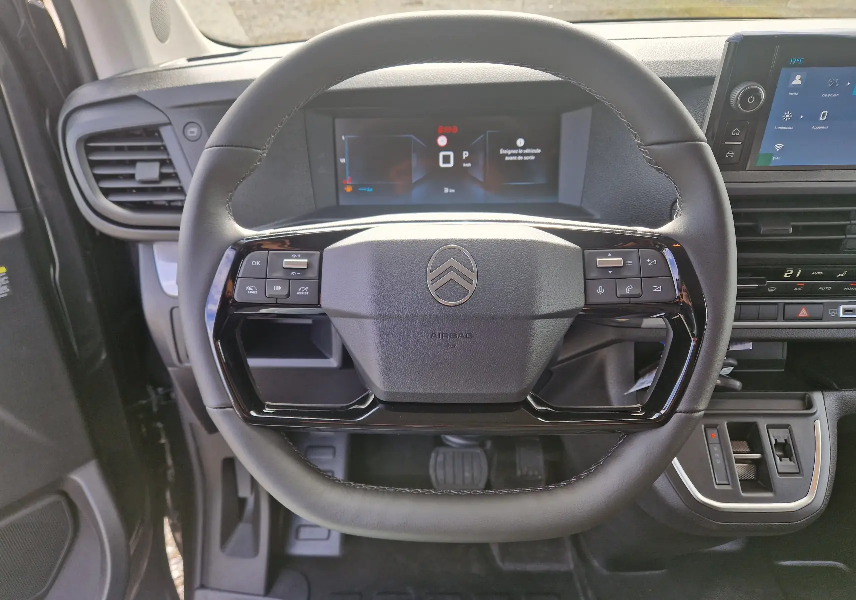 Vue rapprochée du volant cuir noir du Citroën Jumpy XL gris titane, avec tableau de bord numérique et console centrale visible.