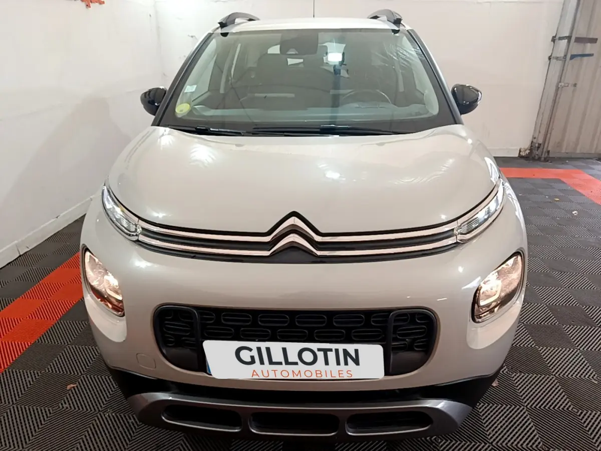 Vue frontale d'un Citroën C3 Aircross blanc avec calandre noire et phares allumés en intérieur showroom.